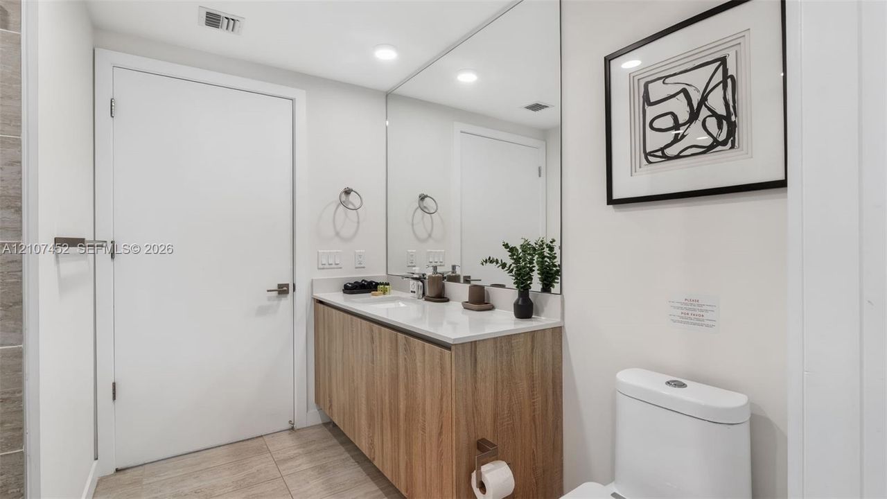 Floating wood-finish vanity with a rectangular sink, stone-surface countertop, floor-to-ceiling wall mirror, and large-format tile flooring