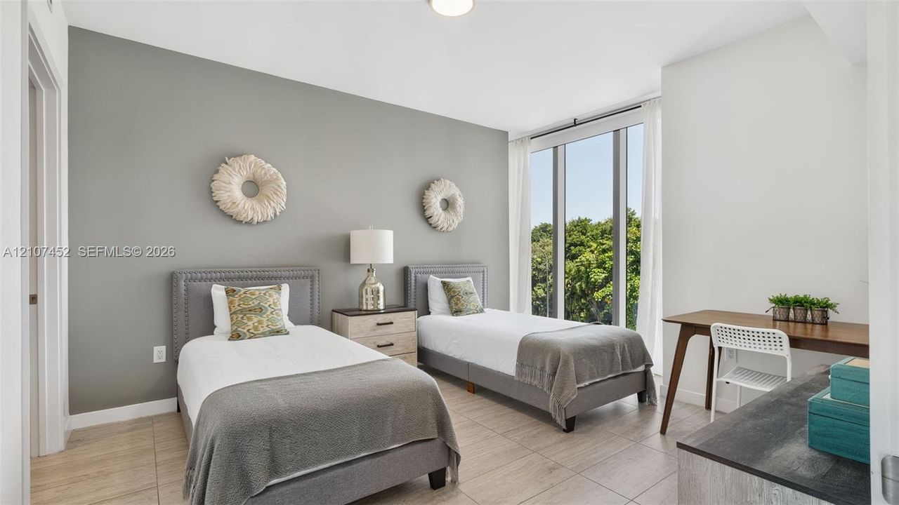 Floor-to-ceiling windows, neutral grey accent wall, and wood-finish tile flooring