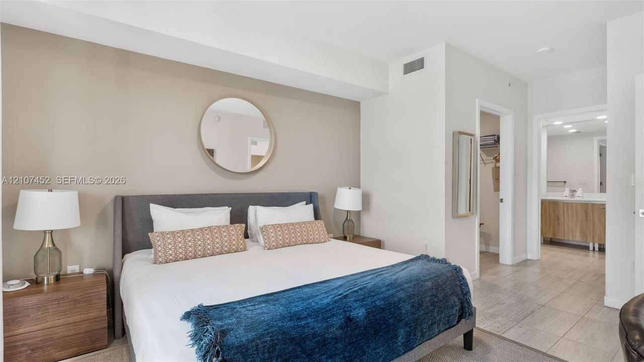 Bedroom featuring neutral wall tones, a circular wall-mounted mirror, and tile flooring