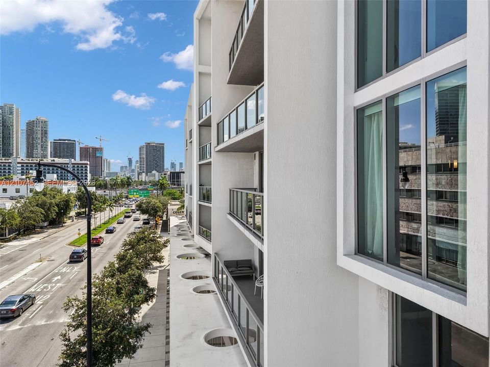Modern multi-story exterior featuring a white stucco facade, floor-to-ceiling windows, and private balconies with glass railings