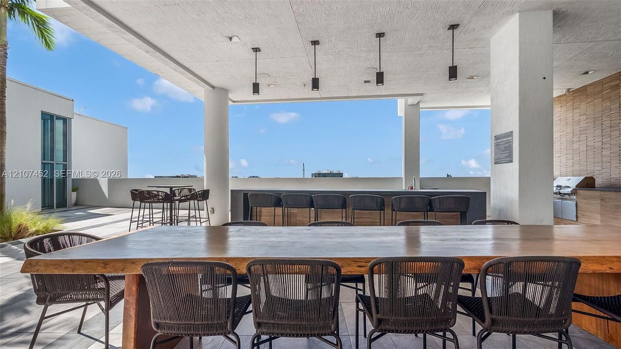 Covered rooftop terrace featuring a built-in outdoor kitchen with stainless steel appliances, a stone-topped bar with integrated seating, and four pendant light fixtures