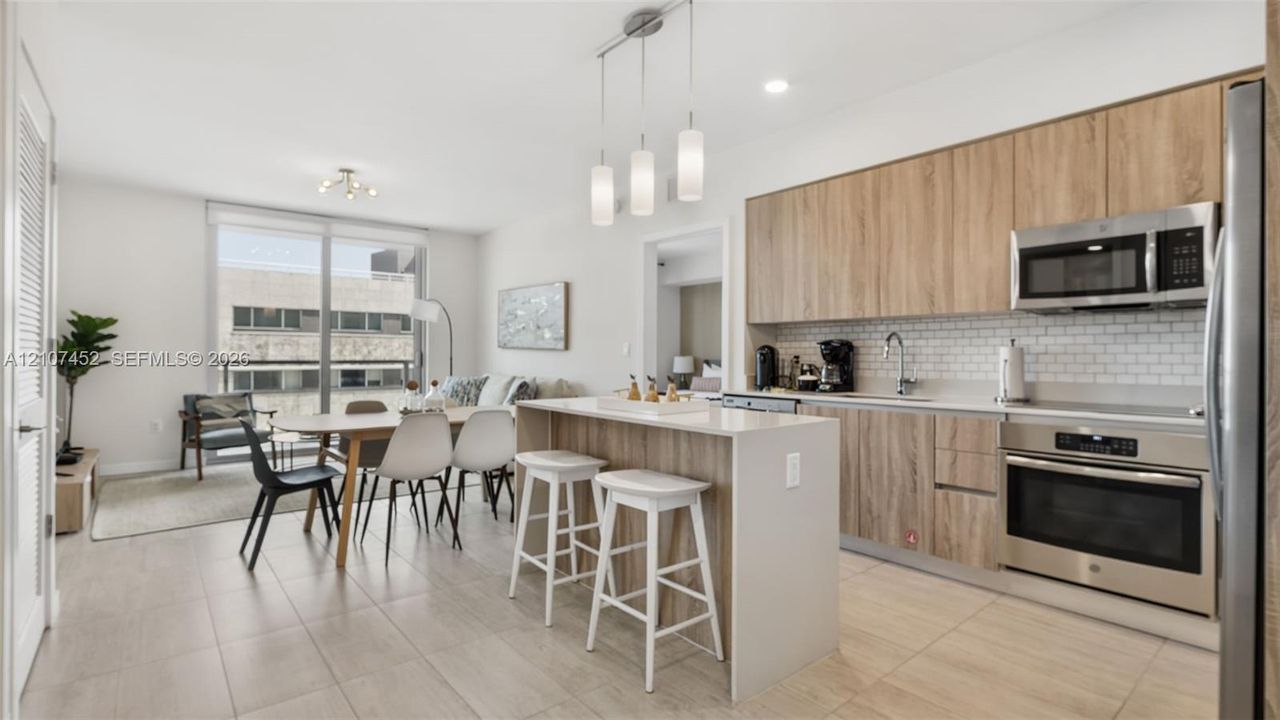 Kitchen featuring wood-finish cabinetry, stone-surface breakfast bar, subway tile backsplash, stainless steel appliances, and tile flooring
