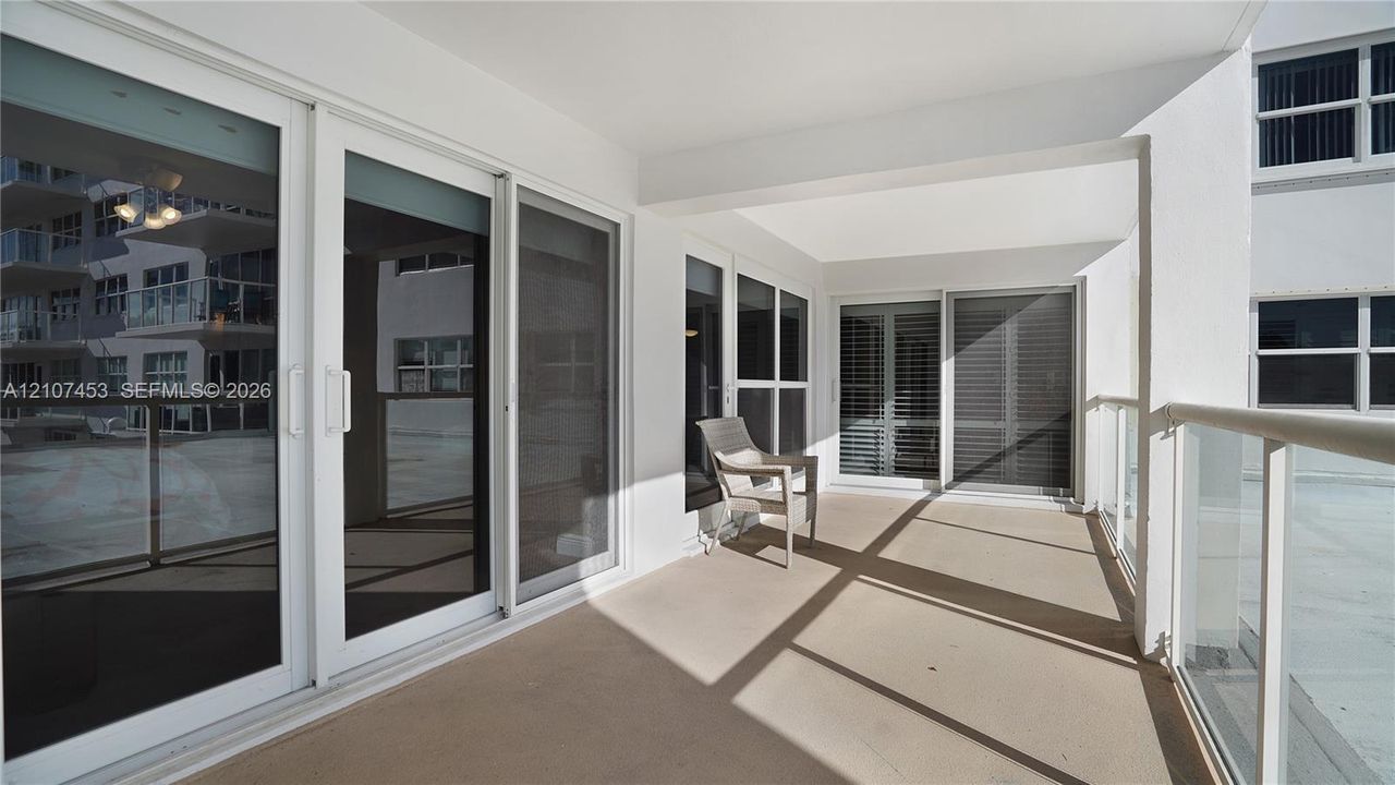 Covered outdoor terrace featuring a concrete floor, floor-to-ceiling glass sliding doors, and a glass-paneled railing