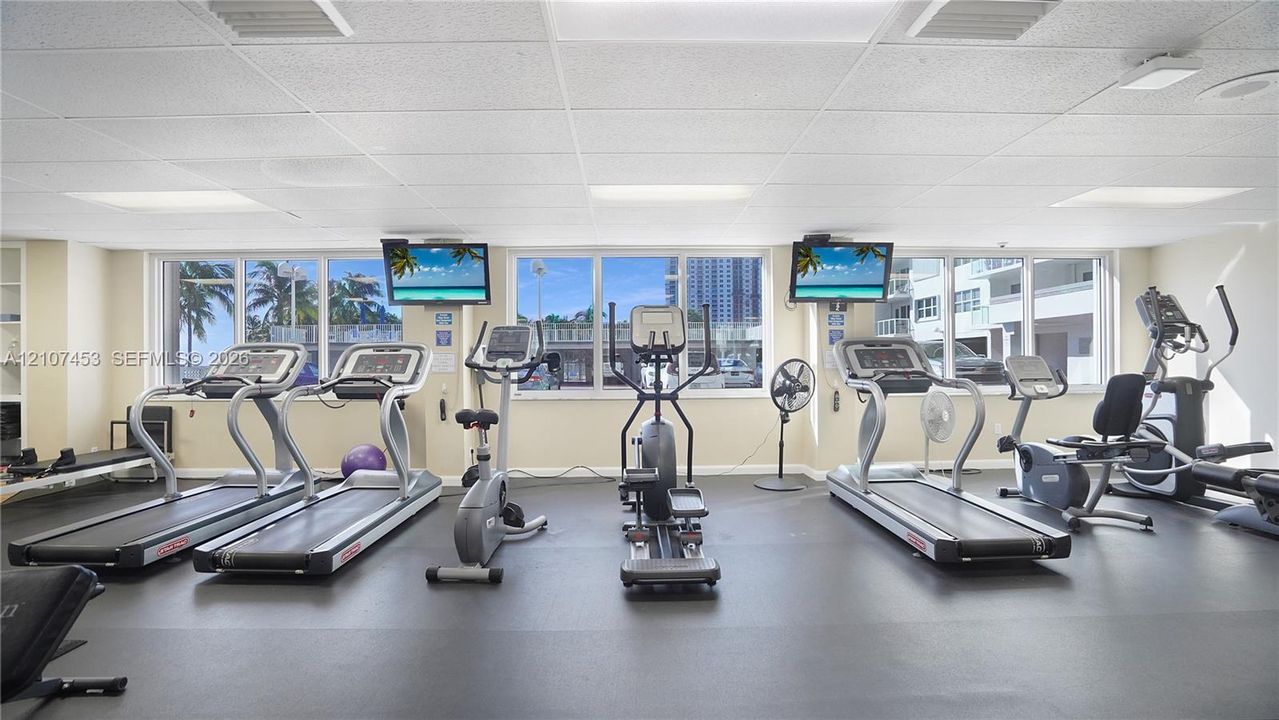Fitness area featuring large-format windows, grid-pattern drop ceiling, and resilient rubber flooring