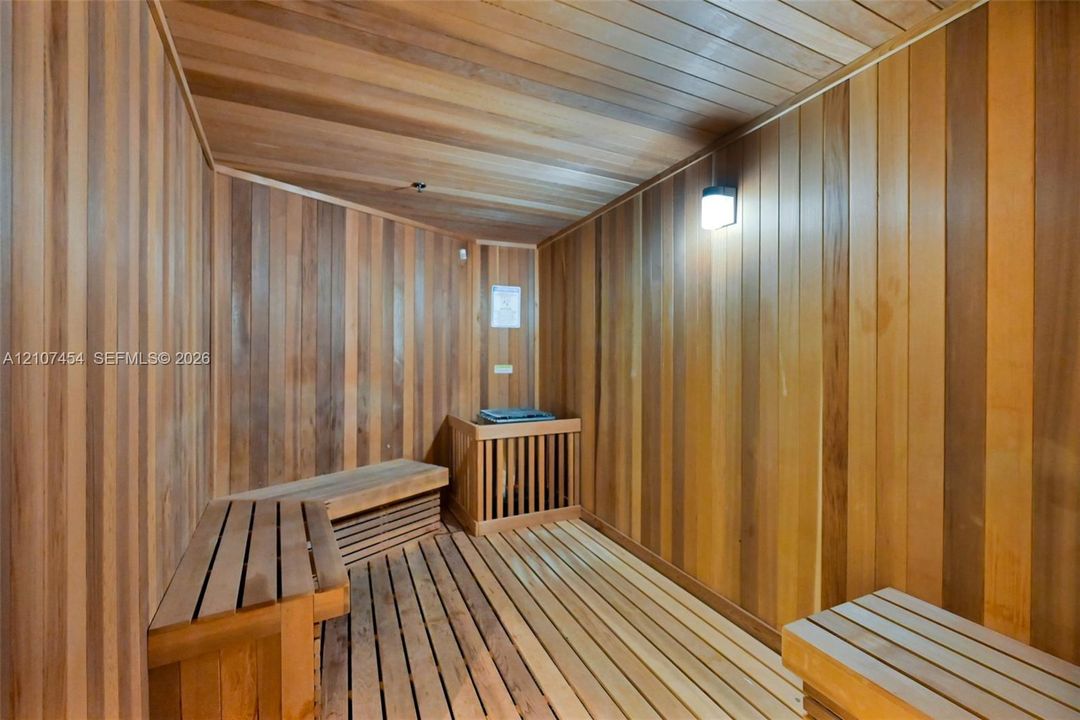 Sauna featuring wood-plank wall paneling, slatted wood-finish flooring, tiered built-in wood bench seating, and integrated wall lighting