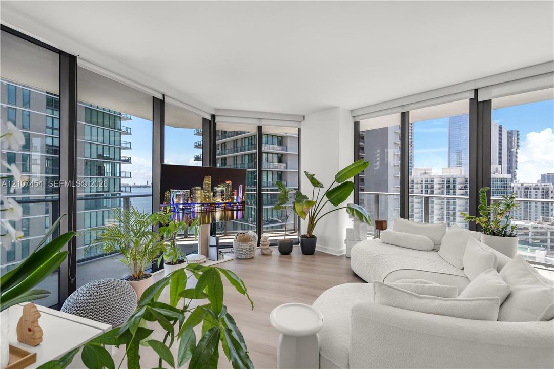 Floor-to-ceiling glass walls, wrap-around balcony with metal railing, and neutral-toned wood-finish flooring