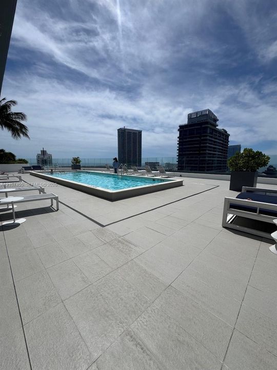 Rooftop terrace featuring a rectangular swimming pool, expansive tile decking, and transparent glass perimeter fencing
