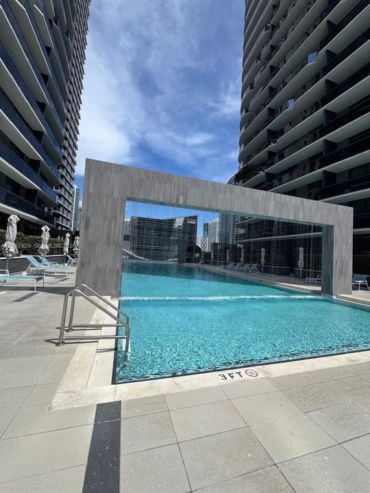Swimming pool featuring an integrated water feature, stone-finish surround, and metal handrails