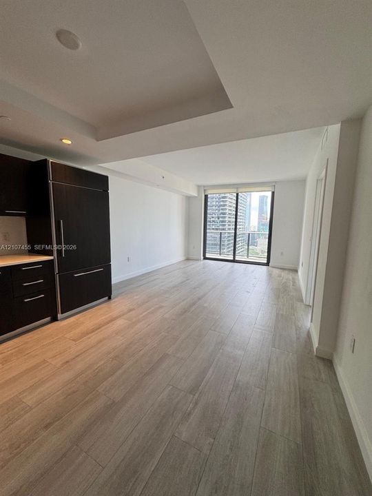 Open-concept living space featuring wood-finish flooring, dark cabinetry, recessed ceiling lighting, and sliding glass doors with balcony access