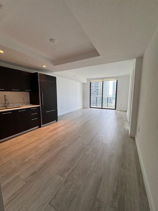 Open-concept interior featuring dark-finish custom cabinetry, integrated refrigeration, wood-finish flooring, recessed ceiling detailing, and floor-to-ceiling glass sliding doors