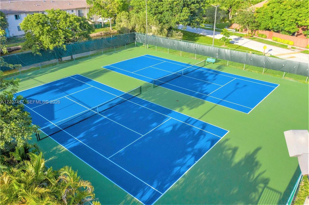 Two tennis courts featuring blue playing surfaces, perimeter fencing, and pole lighting