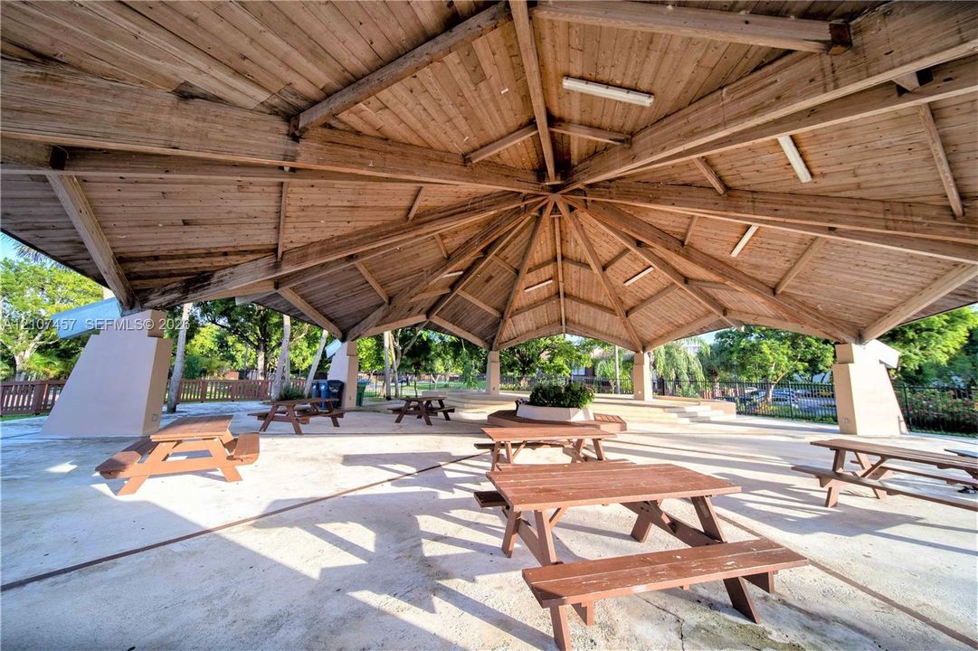 Open-air pavilion featuring a vaulted wood-beam ceiling, concrete flooring, and multiple built-in concrete support pillars