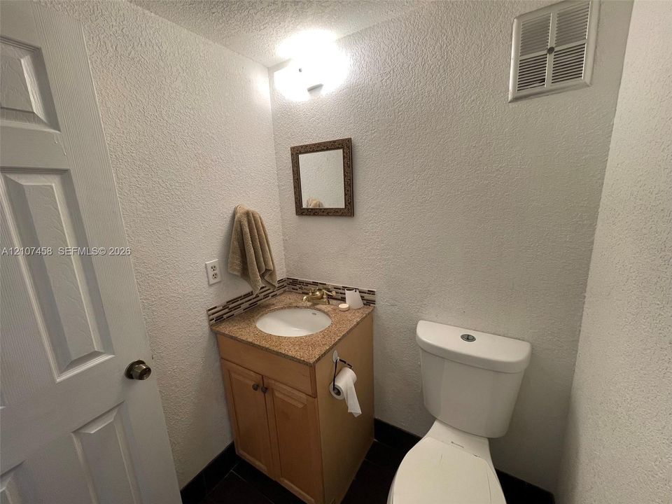 Bathroom featuring a stone-composite countertop, undermount sink, multi-tonal tile backsplash, wood-finish vanity cabinetry, and a wall-mounted vanity mirror