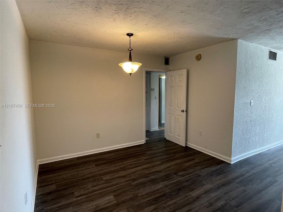 Wood-finish flooring, textured ceiling, and hanging pendant light fixture with a multi-panel interior door