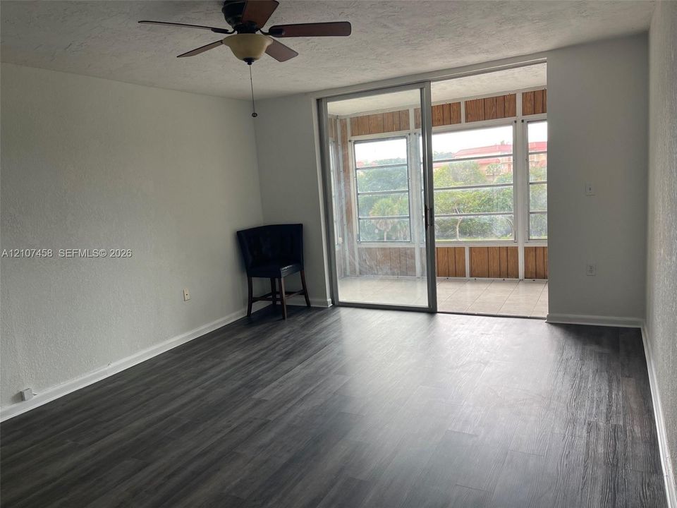 Living area featuring wood-finish flooring, a ceiling fan with integrated lighting, and glass sliding doors opening to a screened-in enclosure with tile flooring and wood-paneled walls