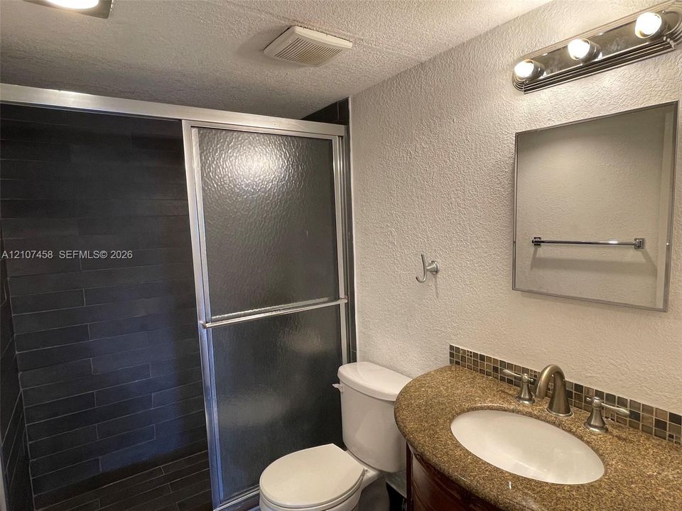 Bathroom featuring a shower stall with dark horizontal tile surround, glass sliding doors, vanity with a curved countertop, integrated oval sink, and mosaic tile backsplash