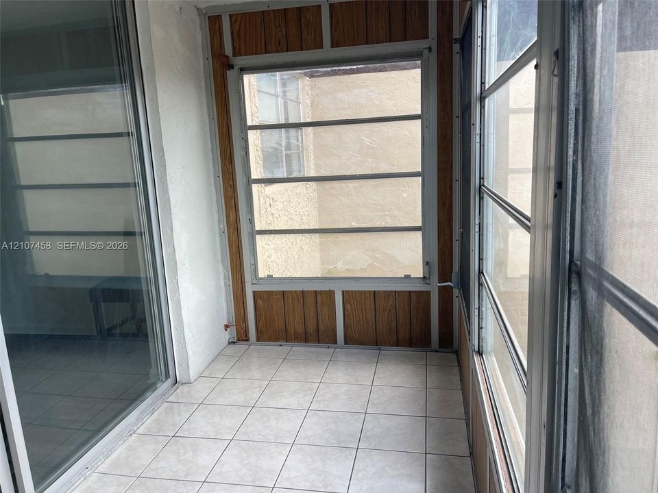 Enclosed porch featuring ceramic tile flooring, wood-panel wall accents, horizontal sliding windows, and a glass sliding door