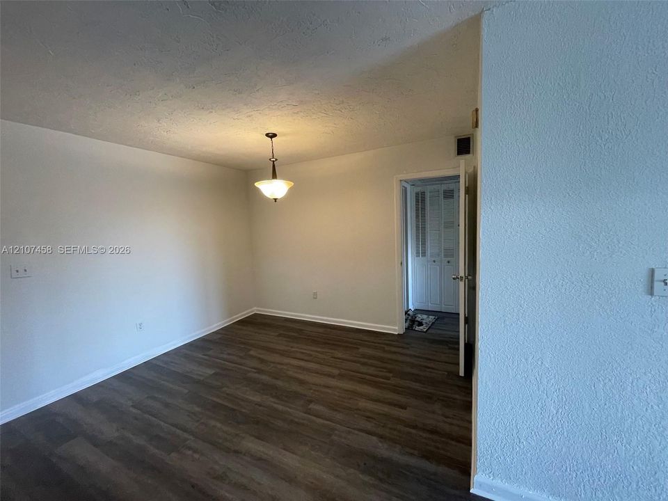 Room featuring wood-finish flooring, a neutral color palette, a classic pendant light fixture, and a doorway leading to a storage closet with louvered doors