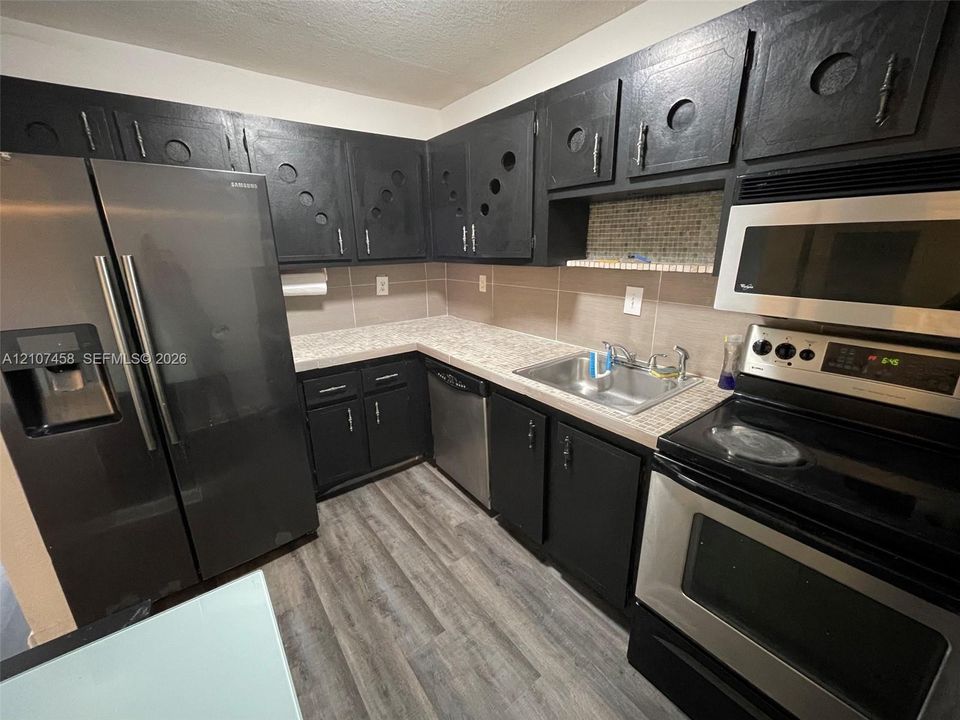 Kitchen featuring custom black cabinetry with circular detailing, stainless steel appliances, patterned laminate countertops, glass tile backsplash, and wood-finish flooring