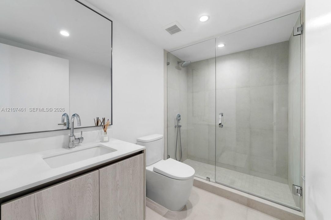 Bathroom featuring a wood-finish vanity with a stone countertop, an integrated rectangular sink, a wall-to-wall mirror, and a walk-in shower with a glass enclosure and tiled walls