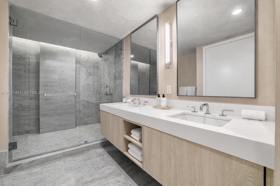 Floating dual vanity with integrated countertop, walk-in shower featuring glass enclosure and stone-tile surrounds, and rectangular wall-mounted mirrors