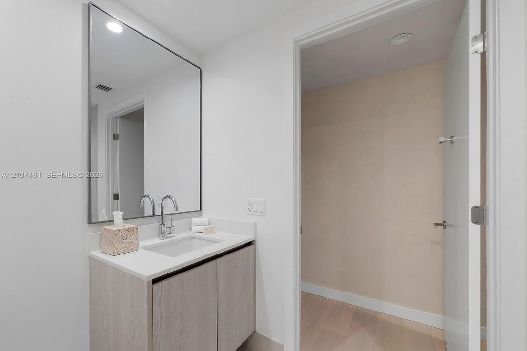 Bathroom vanity featuring light-toned cabinetry, a solid surface countertop with an integrated rectangular sink, a polished chrome bridge faucet, and a large rectangular mirror with a thin metallic frame