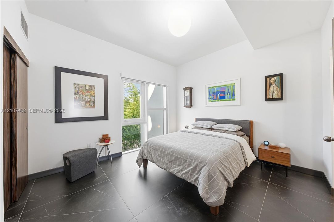 Large-format tile flooring, oversized window with natural light, high ceilings, and wood-finish sliding closet doors