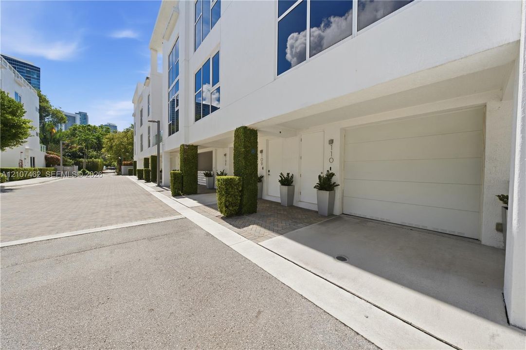 Contemporary multi-story exterior featuring a smooth white stucco finish, floor-to-ceiling windows, integrated garage door, and manicured topiary accents