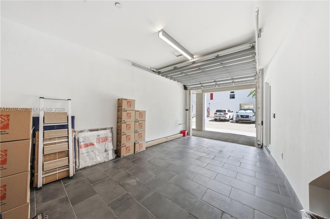 Attached garage featuring large-format tile flooring, white walls, and a linear LED light fixture