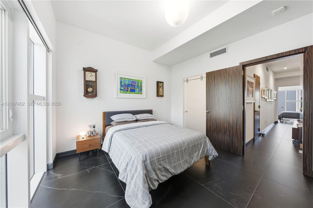 Room featuring large-format dark stone tile flooring, high ceilings, full-height windows, a wooden interior door, and a sliding door