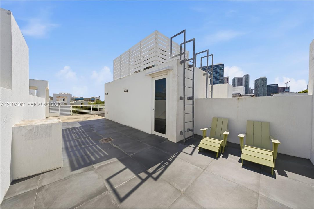 Rooftop terrace featuring oversized tile flooring, white stucco privacy walls, a permanent metal ladder, and built-in privacy screening