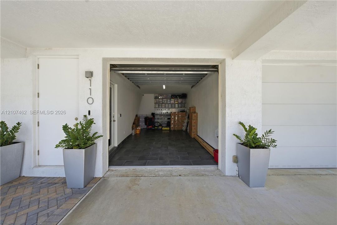 Covered parking area featuring stone-tile flooring, white wall finishes, and direct access to an interior entry door