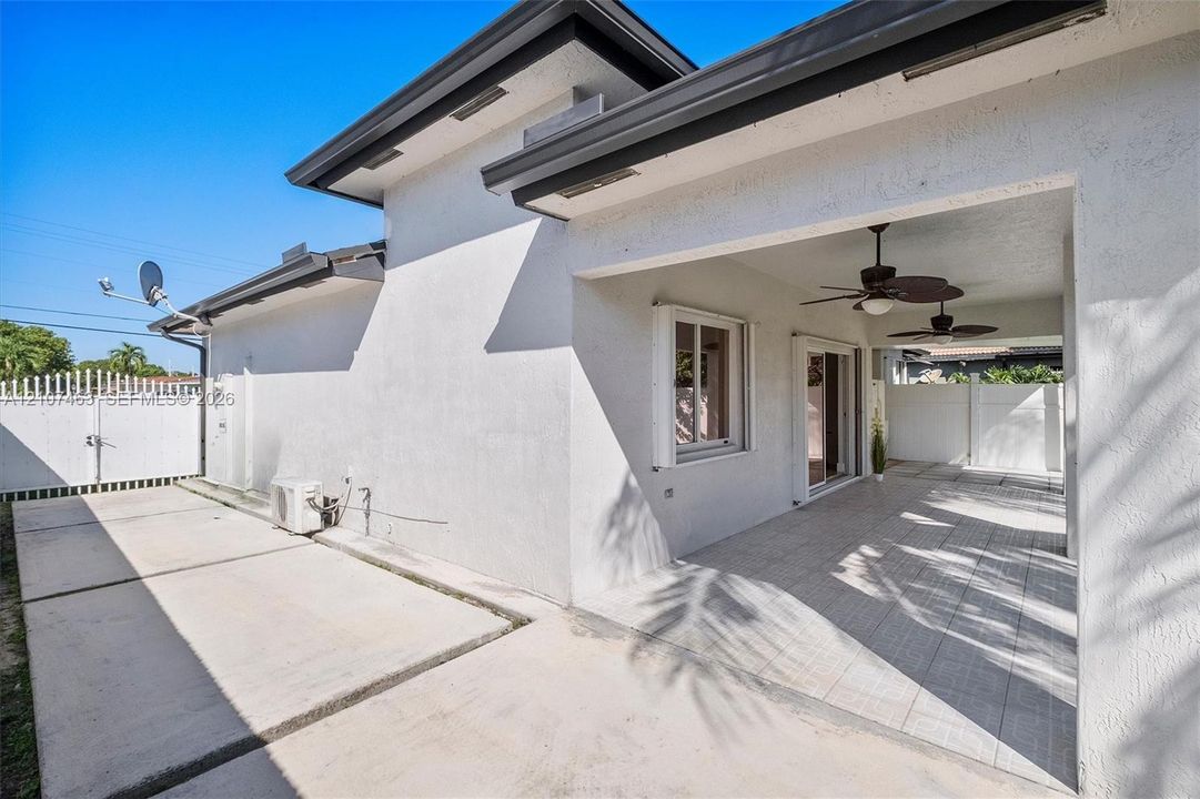 Stucco exterior featuring a covered patio with dual ceiling fans, tile flooring, sliding glass doors, and concrete hardscaping