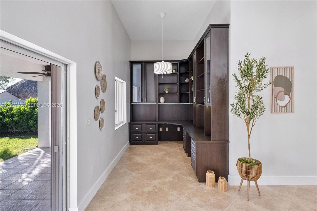 Custom built-in cabinetry with glass-front display shelving and lower drawer storage, stone-finish flooring, vaulted ceilings, and glass sliding doors
