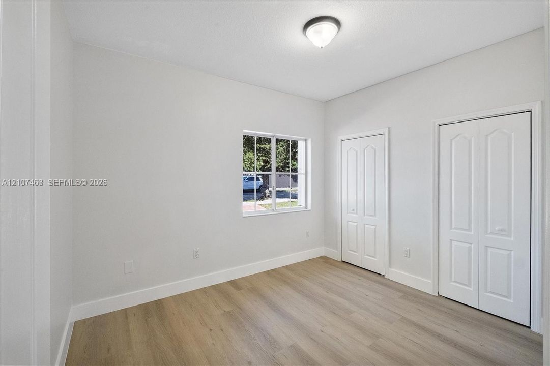 Room 1 featuring wood-finish flooring, a multi-pane window, dual closet doors with arched paneling, and a flush-mount light fixture
