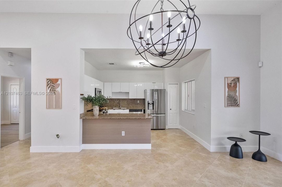 Kitchen featuring high-gloss white cabinetry, stone-finish countertops, stainless steel appliances, tile flooring, and a spherical metal chandelier