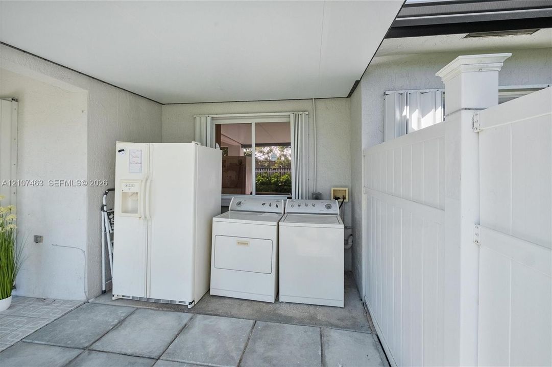 Covered concrete patio featuring laundry area and white vinyl privacy fencing