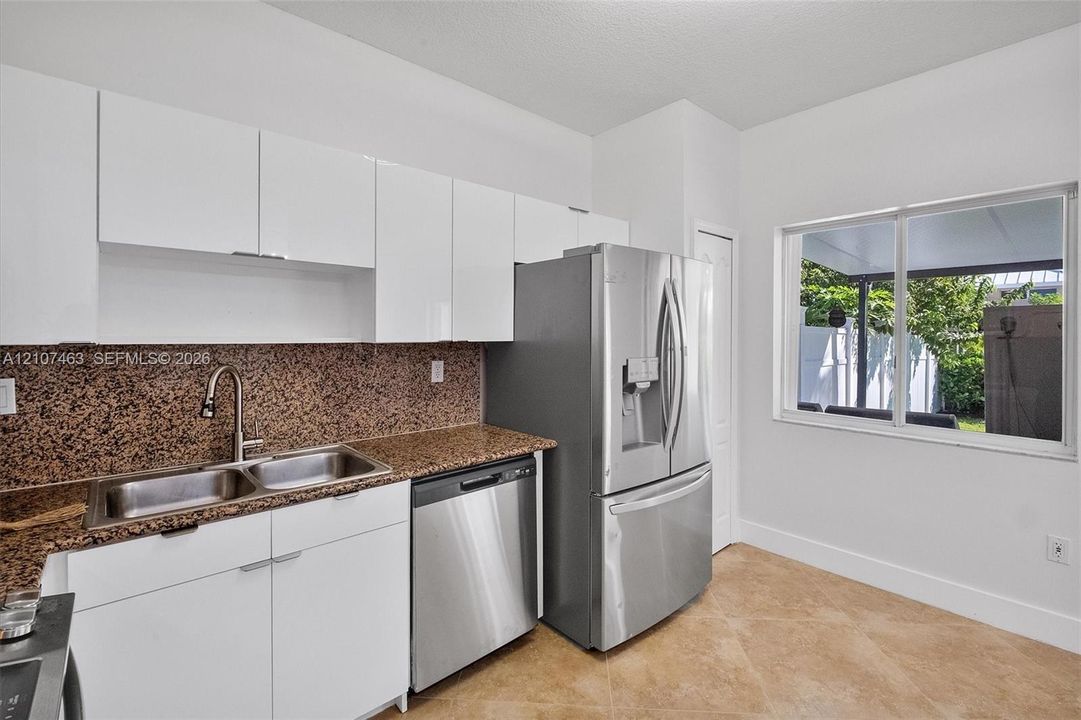 Kitchen featuring flat-panel white cabinetry, stone-finish countertops, stainless steel appliances, a dual-basin undermount sink with a gooseneck faucet, and tile flooring