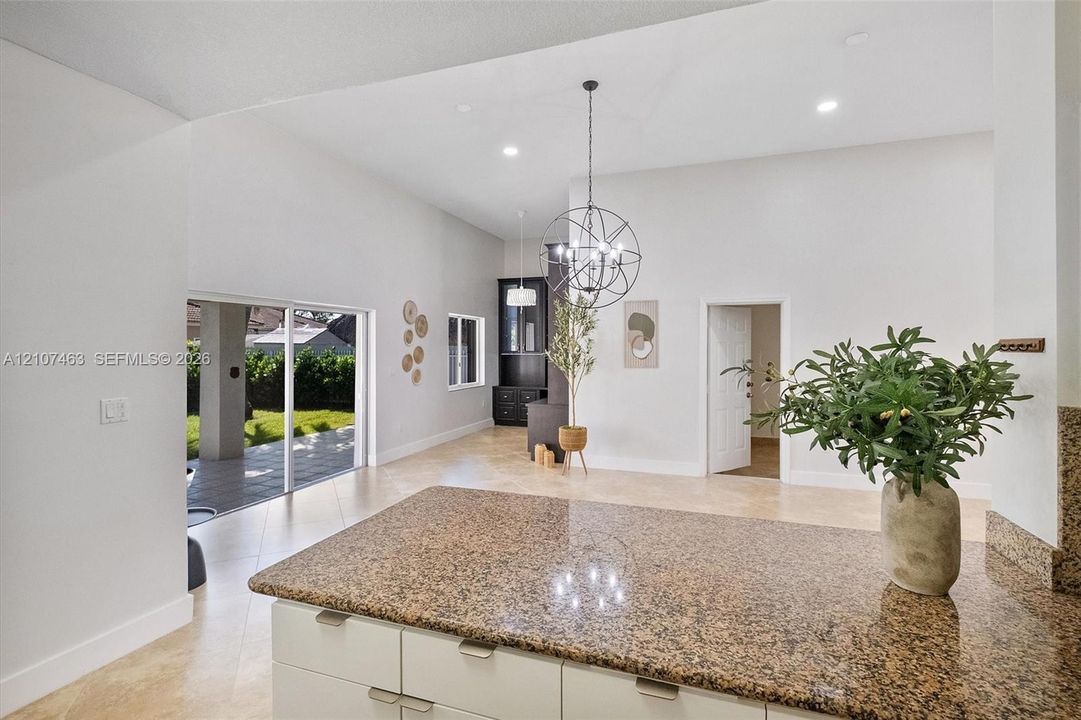 Open-concept kitchen and living area featuring high vaulted ceilings, stone-finish countertops, tile flooring, recessed lighting, and a spherical metal chandelier