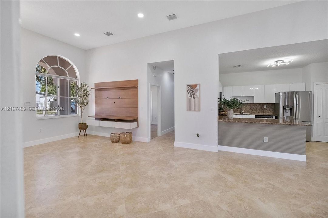 Open-concept living space featuring high ceilings, recessed lighting, tile flooring, an arched window, and a built-in media console