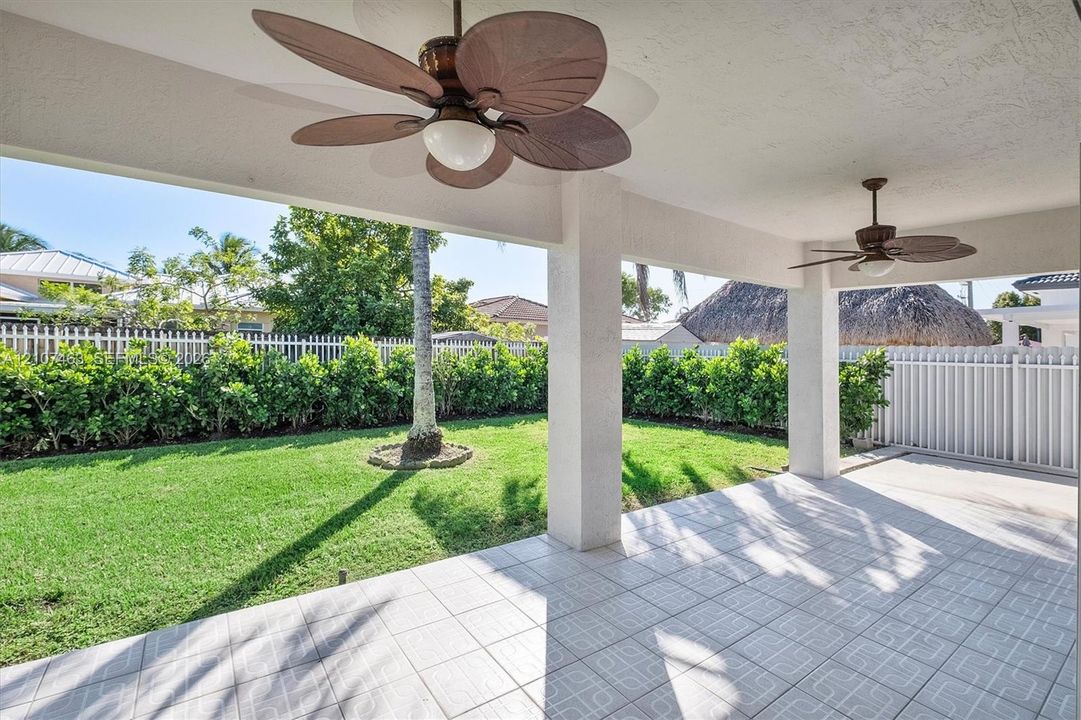 Covered patio featuring ceramic tile flooring, twin ceiling fans with light fixtures, and structural support columns