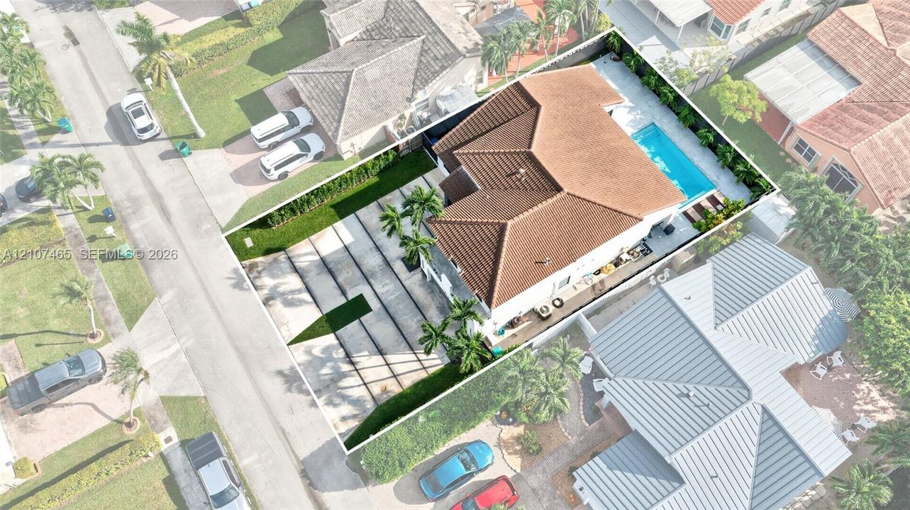 Aerial perspective featuring a tile roof, concrete driveway, and a private swimming pool set within a perimeter-fenced yard