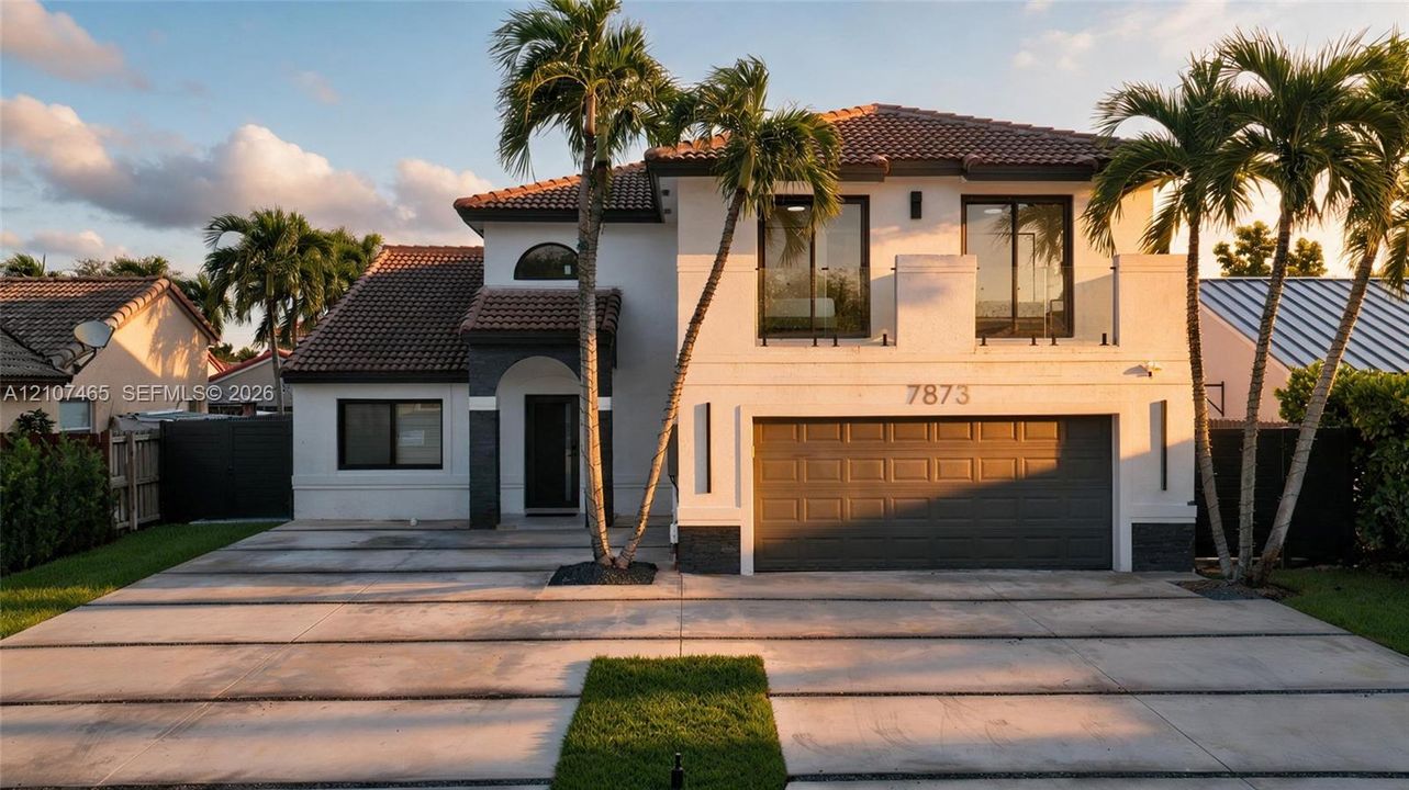 Stucco exterior featuring a tiled roof, arched entryway, second-story balcony with glass railing, and multi-panel garage door