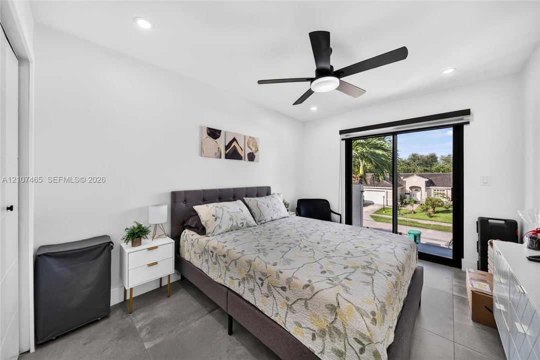 Room featuring large-format tile flooring, matte black ceiling fan with integrated lighting, and sliding glass door with a black frame