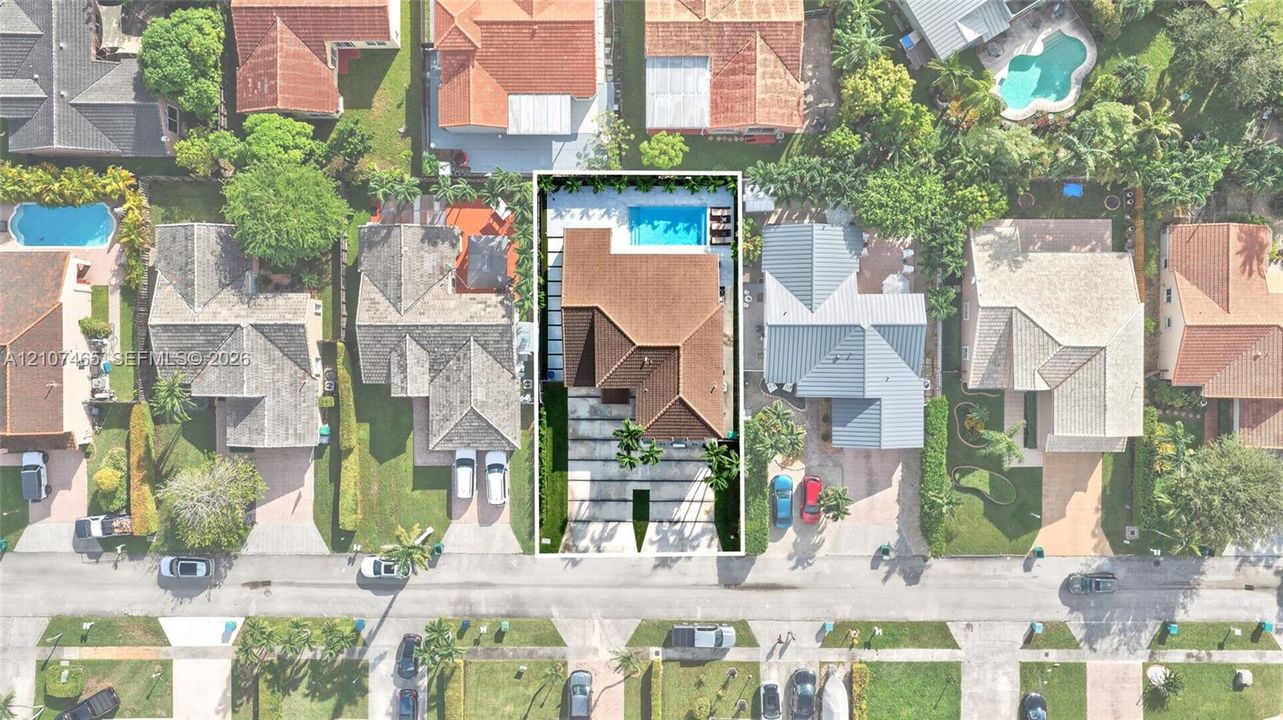 Aerial perspective of residential property featuring a tiled roof, concrete paver driveway, manicured lawn, and a rectangular swimming pool