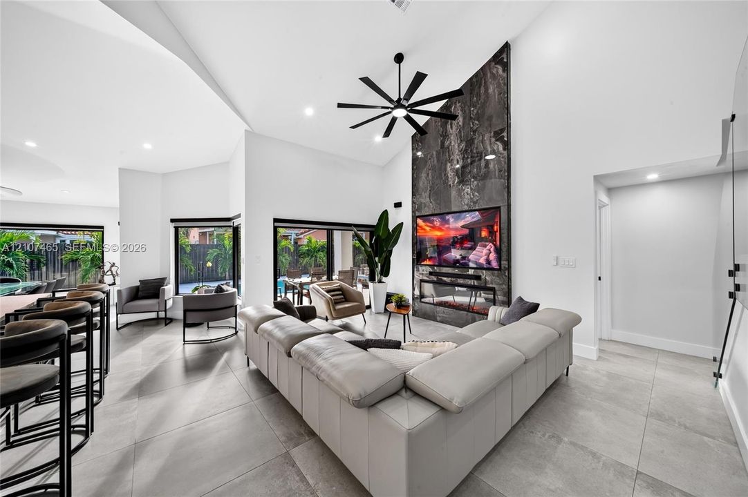 Open-concept living area featuring vaulted ceilings, large-format tile flooring, a floor-to-ceiling stone fireplace surround with a linear electric insert, and sliding glass doors