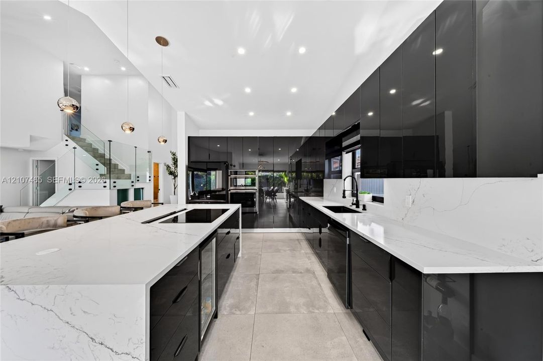 Modern kitchen featuring high-gloss cabinetry, stone-surface countertops with waterfall edge, integrated cooktop, matte black fixtures, and large-format tile flooring