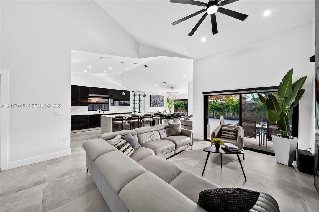 Vaulted ceilings, large-format tile flooring, matte black ceiling fan, recessed lighting, and expansive sliding glass doors
