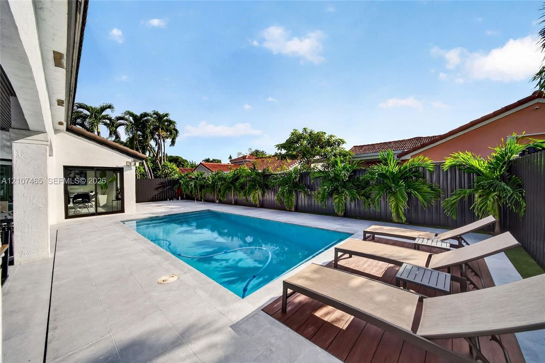 In-ground swimming pool with stone-tile decking, wood-finish decking accents, and perimeter privacy fencing