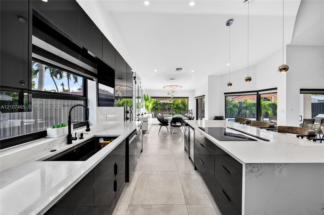 High-gloss cabinetry, quartz countertops with waterfall edge, large-format tile flooring, recessed lighting, and modern pendant fixtures